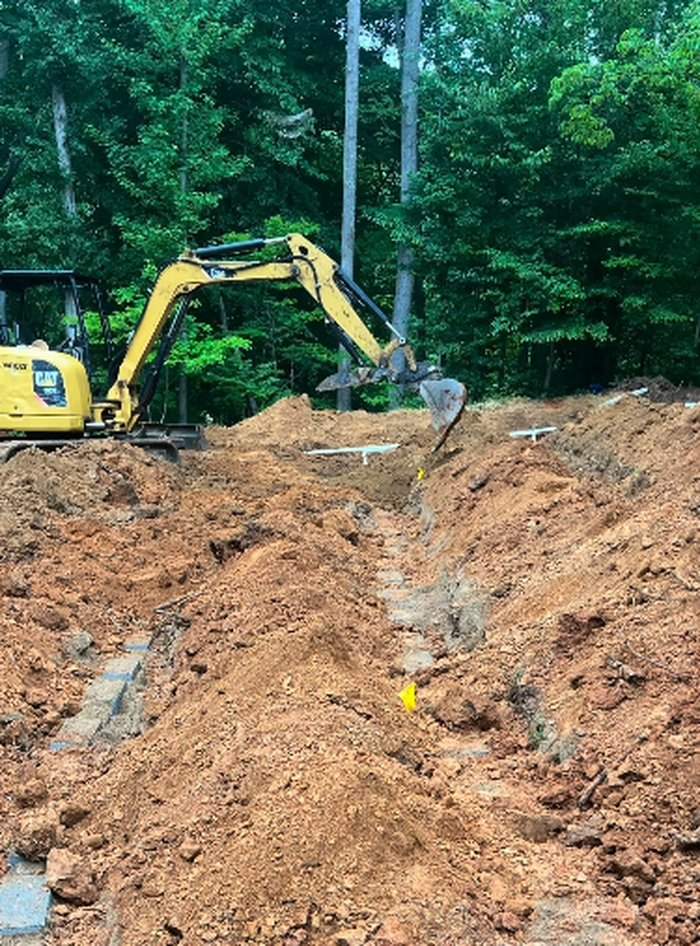 Excavator digging a septic line trench beside a distribution box